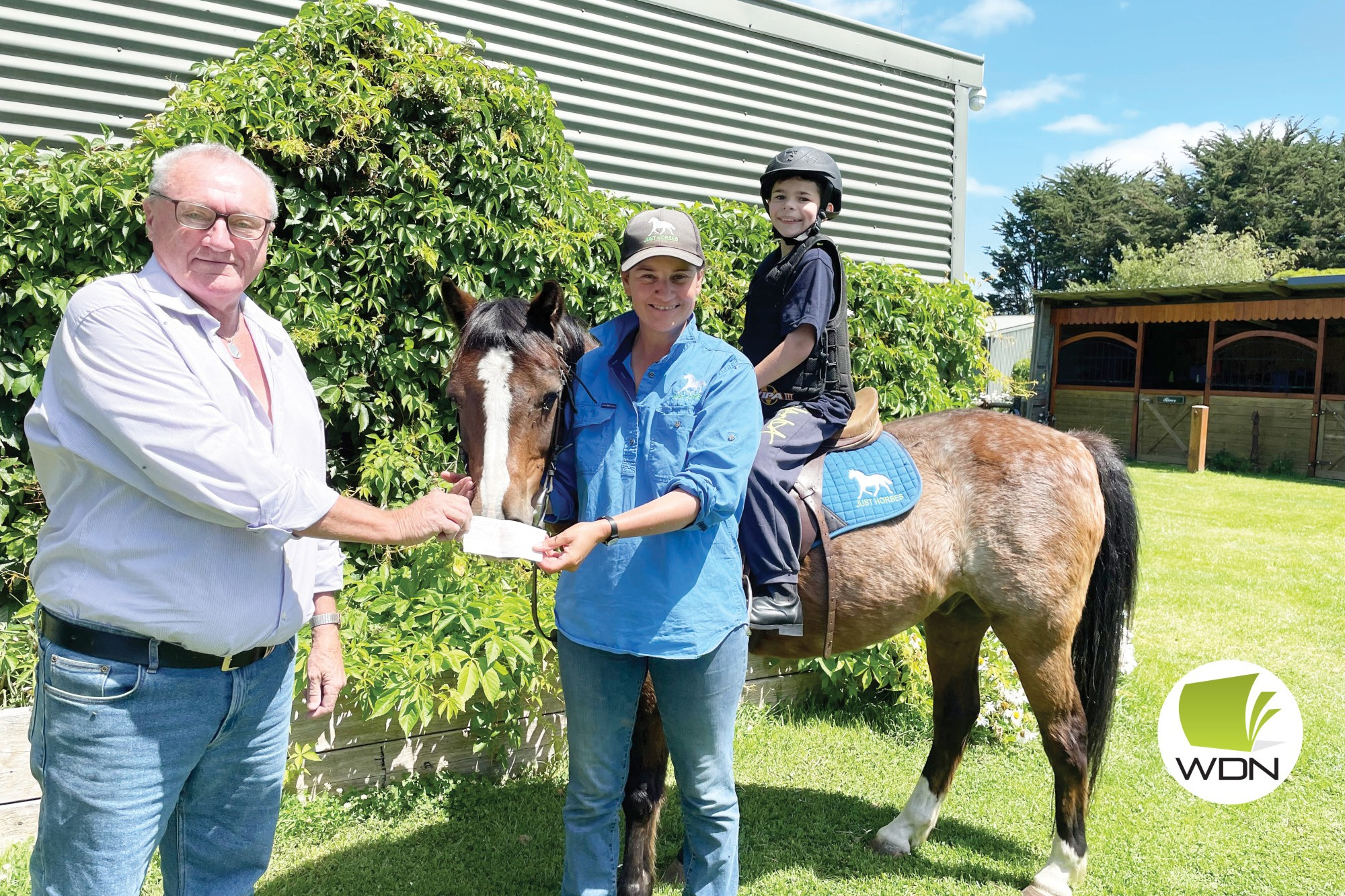 Working together: Hampden Social Club president Laurie O’Neill presents Just Horses owner Andrea Bell with a cheque to help upgrade safety equipment for program participants like Thomas Mitchell on equine therapy horse, River.