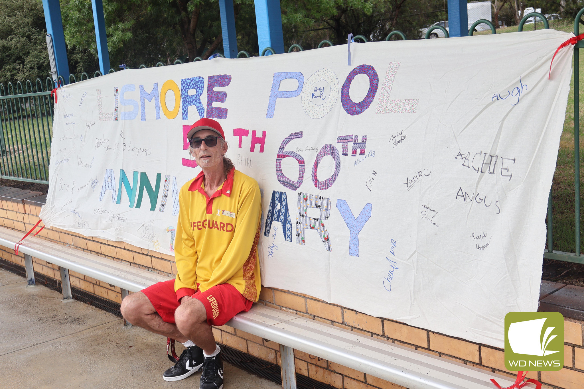 Happy birthday: Lismore Pool manager Nigel Hooker sits with the updated birthday banner, which was used when the pool turned 50, while looking back on those who signed it 10 ago.